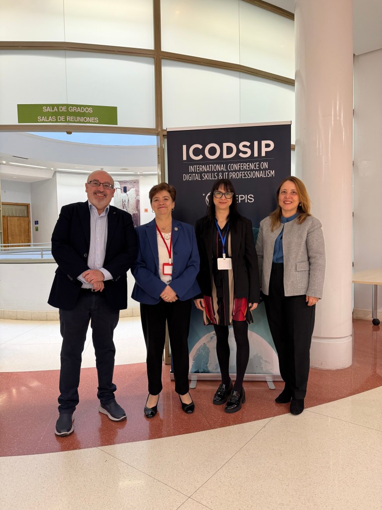 Four people standing in front of a conference banner